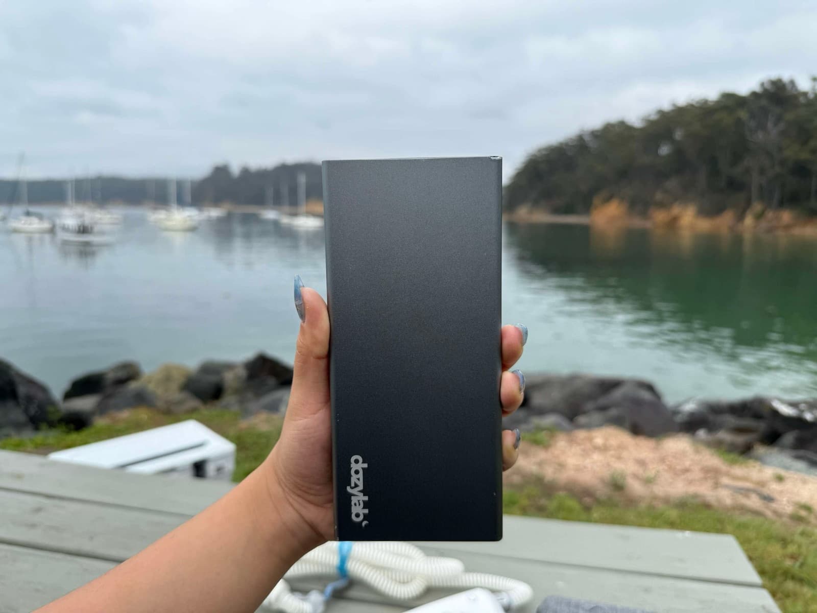 Portable battery held up beside a calm waterfront